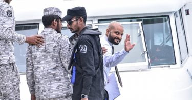 Dhiggaru MP Faris Maumoon waves as he is escorted to jail. PHOTO/MIHAARU