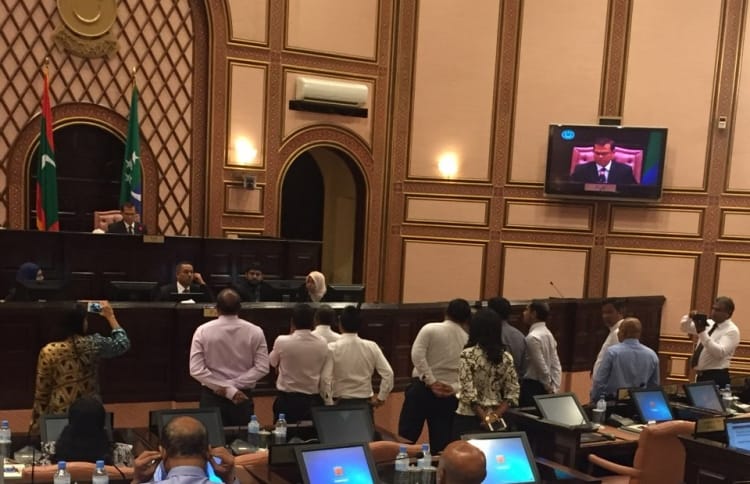 Speaker Abdulla Maseeh addresses the first sitting of 2017's third term of the parliament from his elevated seat behind a wooden "wall", while opposition lawmakers protest and call on him to step down.
